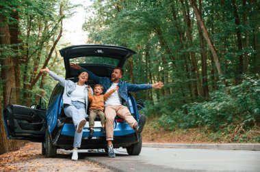 Mutlu bir aile. Anne, baba ve küçük oğlu dışarıda elektrikli araba bekliyor..