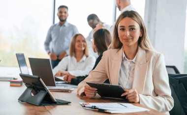 Masada not defteri ve tableti olan bir kadın var. Bir grup ofis çalışanı içeride birlikte..