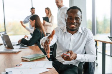 Dost canlısı siyah adam elini sıkmak için uzatıyor, selamlar. Bir grup ofis çalışanı içeride birlikte..