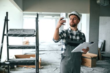 Projeyi planlıyorum, kağıtlarla. Bitmemiş odada üniformalı inşaat işçisi..