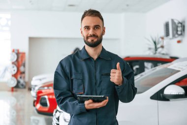 Ayakta durup tableti tutarak. Araba tamircisi otomobille garajda..
