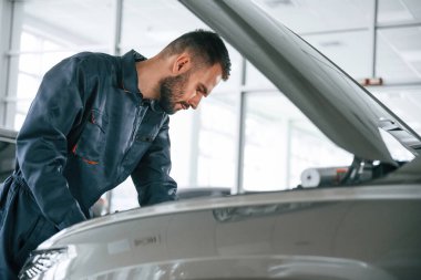 Yan görüş, kaput açık. Araba tamircisi otomobille garajda..