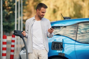 Ön manzara. Şarj istasyonunda mavi elektrikli arabası olan adam..