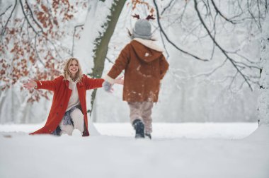 Geyik boynuzları olan bir şapka. Anne ve kızı kış çayırlarında ve ormandalar..