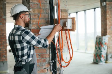 Elektrikle çalışıyor. Bitmemiş odada üniformalı bir inşaat işçisi var..