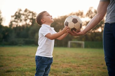 Çocuk futbol topunu alıyor. Baba ve küçük oğlu dışarıda oynuyor ve eğleniyorlar..