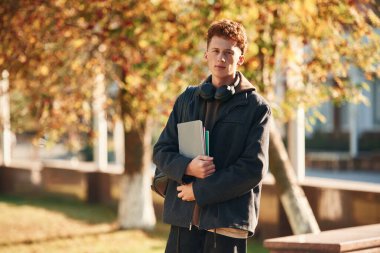 Ayakta ve not defterini tutarak. Genç öğrenci üniversitenin dışında, siyah elbiseli..