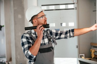 El feneri kullanıyor. Üniformalı tamirci tamamlanmamış binada..