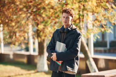 Ayakta ve not defterini tutarak. Genç öğrenci üniversitenin dışında, siyah elbiseli..