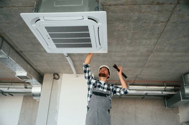 El feneri kullanıyor. Üniformalı tamirci tamamlanmamış binada..