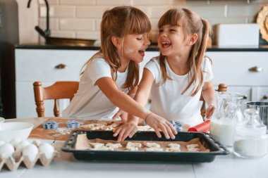 Gülümseyen, neşeli bir ruh hali. İki küçük kız mutfakta çelenklerle yemek hazırlıyor..