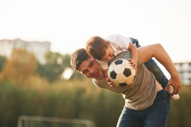 Profesyonel futbol topunu tutuyor. Baba ve küçük oğlu dışarıda oynuyor ve eğleniyorlar..