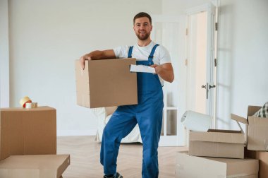 Kameraya bakıyor, kutuyu tutuyor. Servis elemanını bir odaya taşımak.