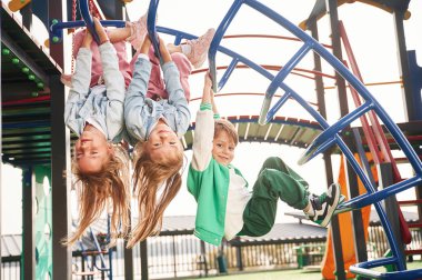 Baş aşağı asılı duruyor. Çocuklar oyun alanında eğleniyor..