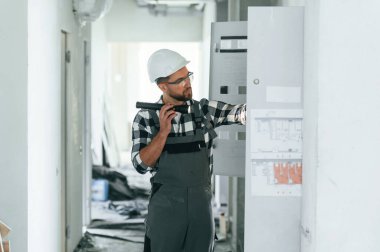 Yan görüş, el feneri kullanmak, elektrik kutusunu kontrol etmek. Üniformalı tamirci tamamlanmamış binada..
