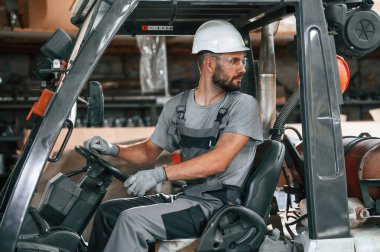 Forklift sürüyorum. Gri üniformalı genç fabrika işçisi.