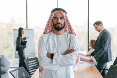 O arkadaki insanların önünde durmak. Geleneksel kıyafetli Müslüman işadamı ve görevde meslektaşları.