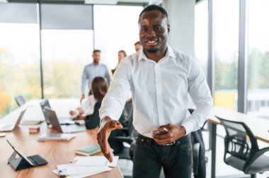 Dost canlısı siyah adam elini sıkmak için uzatıyor, selamlar. Bir grup ofis çalışanı içeride birlikte..
