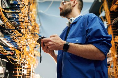 Profesyonel cihaz ellerinde. Genç adam sunucu odasında internet ekipmanı ve kablolarıyla çalışıyor..