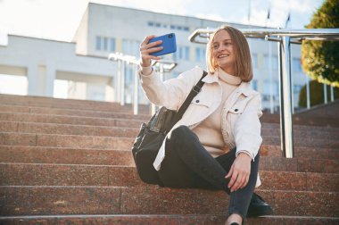 Akıllı telefondan selfie çekiyoruz. Gündelik giysiler içinde genç bir kız öğrenci dışarıda..