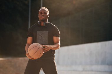 Fotoğraf hareket halinde. Genç siyah adam basketbol topuyla dışarıda..
