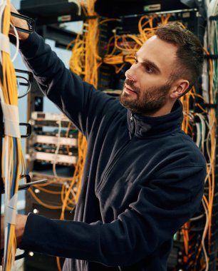 Siyah kıyafetler. Genç adam sunucu odasında internet ekipmanı ve kablolarıyla çalışıyor..