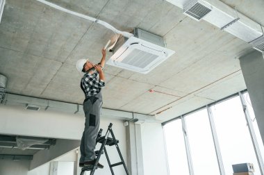 Havalandırma sistemi tamir ediliyor. Üniformalı tamirci tamamlanmamış binada..