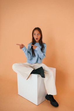 Oturup parmaklarıyla gösteriyordu, şok olmuştu. Şirin genç kız stüdyoda arka planda..