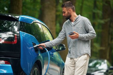 Genç adam şarj aletini elektrikli otomobil soketine takıyor..