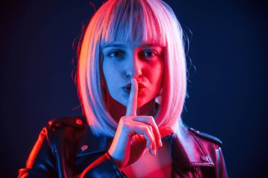 Parmaklar dudaktan, sessizlik. Beyaz saçlı kadın stüdyoda neon renkli..