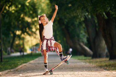 Kulakları olan sevimli pembe kulaklıklarla. Dışarıda kaykaylı mutlu küçük kız.