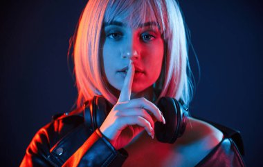 Sessiz olmanın işareti, parmak dudaklardadır. Beyaz saçlı kadın stüdyoda neon renkli..