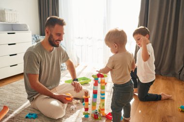 Babam yerde oyuncaklarla oynayan iki küçük çocukla oynuyor..