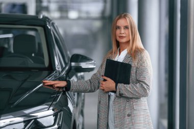 Elinde tabletle. Resmi kıyafetli kadın araba galerisinde..