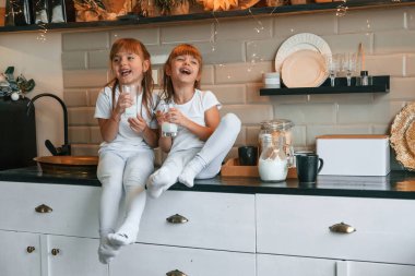 Halkın refahı. Mutlu iki küçük kız mutfaktaki masada otururken süt içiyor..
