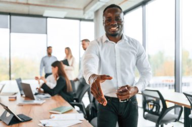 Dost canlısı siyah adam elini sıkmak için uzatıyor, selamlar. Bir grup ofis çalışanı içeride birlikte..
