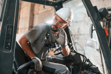 Profesyonel forklift sürücüsü. Gri üniformalı genç fabrika işçisi.