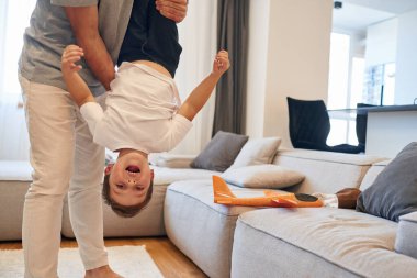 Çocuğu baş aşağı tutmak. Adam evcil odasında oğluyla oynuyor..