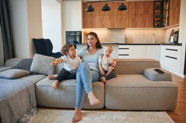 Anne ve iki erkek çocuğu evdeki kanepede oturuyor..