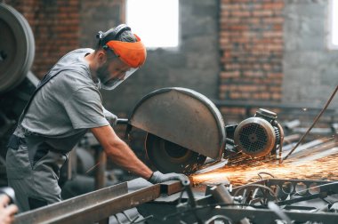 Yan görünüş, metali kesmek. Gri üniformalı genç fabrika işçisi.