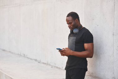 Boynunda kulaklıkla. Yakışıklı siyah adam gündüz vakti dışarıda poz veriyor..