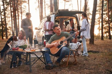 Akustik gitarist. Arkadaş gurubu ormanda bir arada..