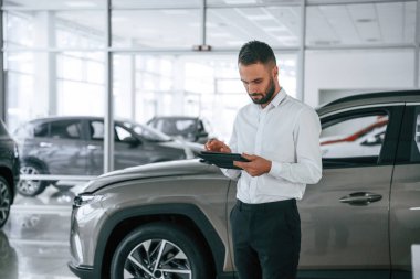 Siyah renkli tablet ellerinde. Resmi giyinen işçi oto kuaföründe..