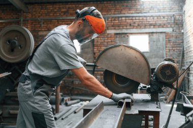Metali kesme işlemi. Gri üniformalı genç fabrika işçisi.
