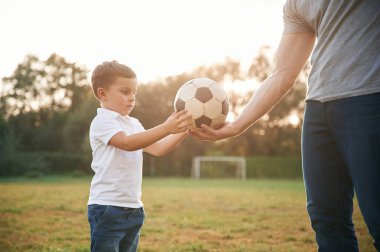 Çocuk futbol topunu alıyor. Baba ve küçük oğlu dışarıda oynuyor ve eğleniyorlar..