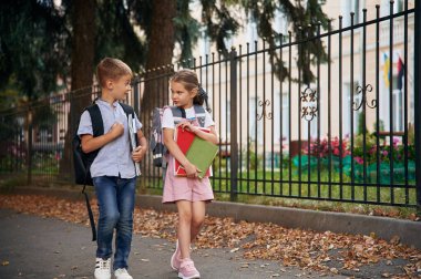 Defter ve kitap tutuyor. Erkek ve kız çocuklarının çocukları dışarıda birlikteler..