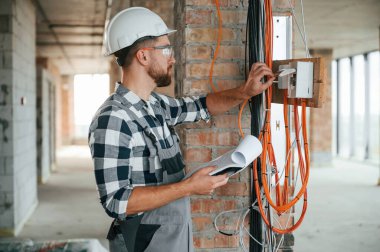 Elektrikle çalışıyor. Bitmemiş odada üniformalı bir inşaat işçisi var..