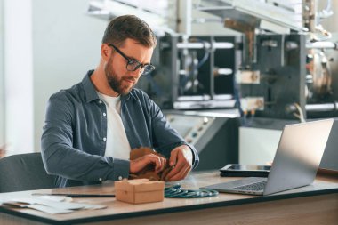 Resmi kıyafetler ve bardaklar, masanın yanında. Yakışıklı adam ekolojik kutular üreten fabrikada çalışıyor..