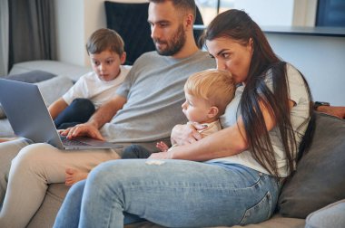 Bacaklarında dizüstü bilgisayarla. İki küçük çocuklu ebeveynler evcil odada birlikteler..