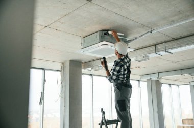 Havalandırma sistemi tamir ediliyor. Üniformalı tamirci tamamlanmamış binada..